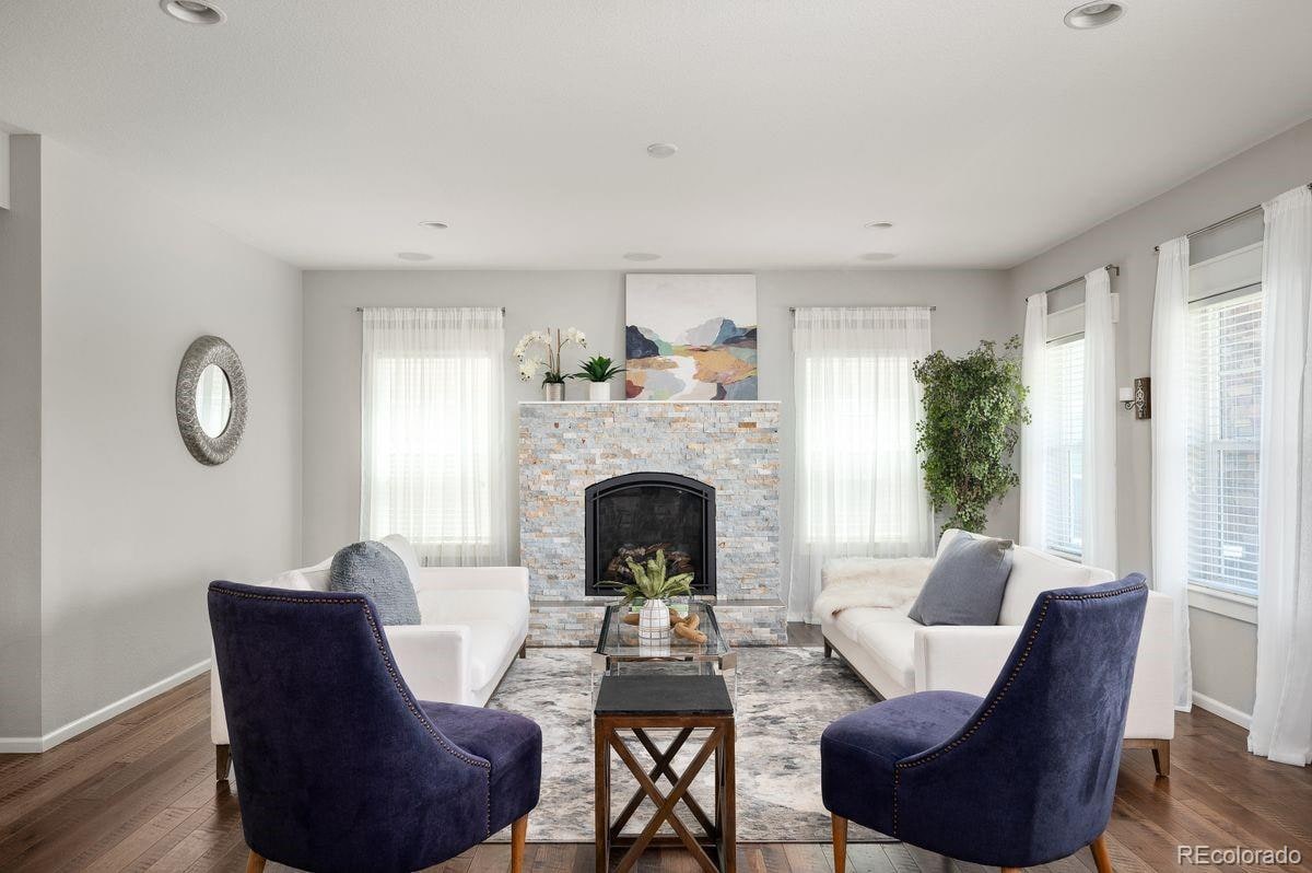 Staged living room with a stone fireplace, two navy chairs, greenery, and a clear central sightline